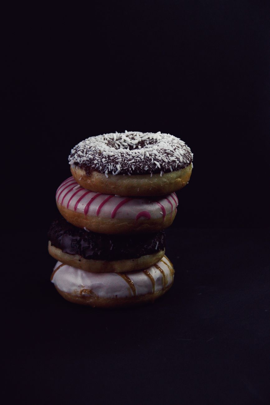 Sweet appetizing donuts with glaze and coconut flakes stacked above each other.
