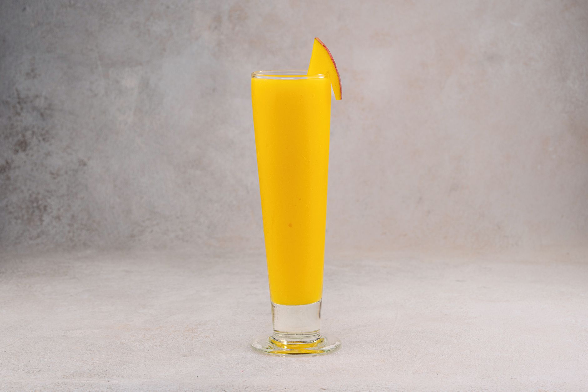 Bright mango smoothie in a tall glass with a mango slice. Perfect for food photography.