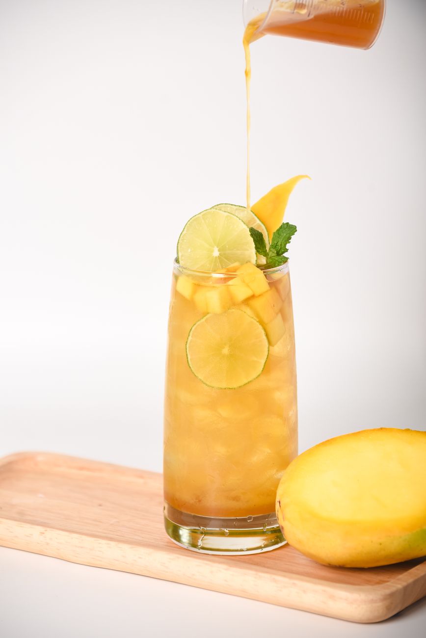A tall glass of mango juice garnished with lime slices and mint on a wooden tray.