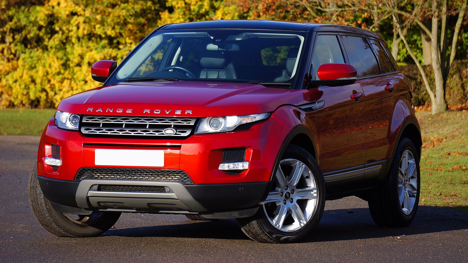 Bright red Range Rover SUV parked outdoors on a sunny autumn day.