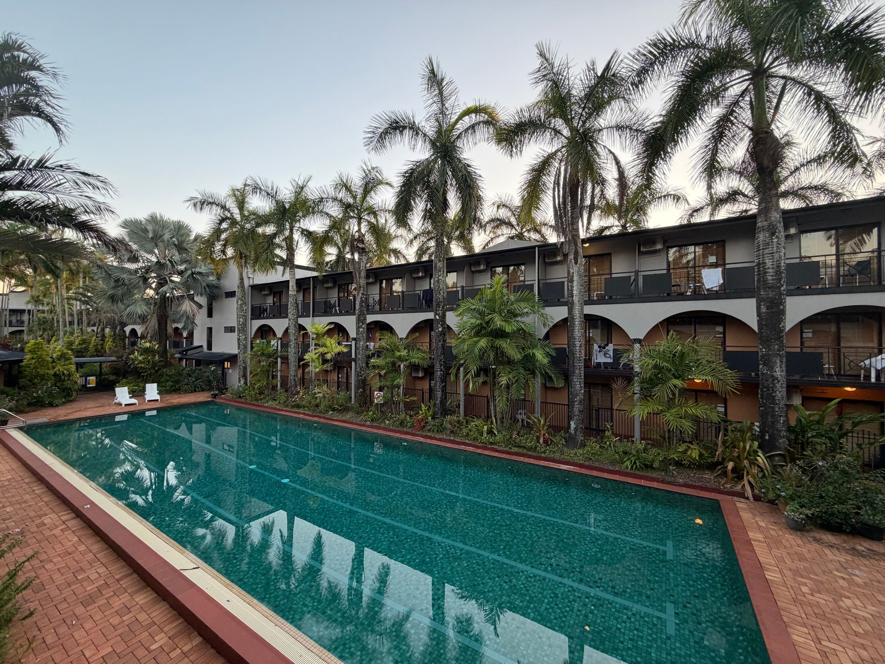 Serene tropical resort with a lush palm-lined swimming pool at sunrise.